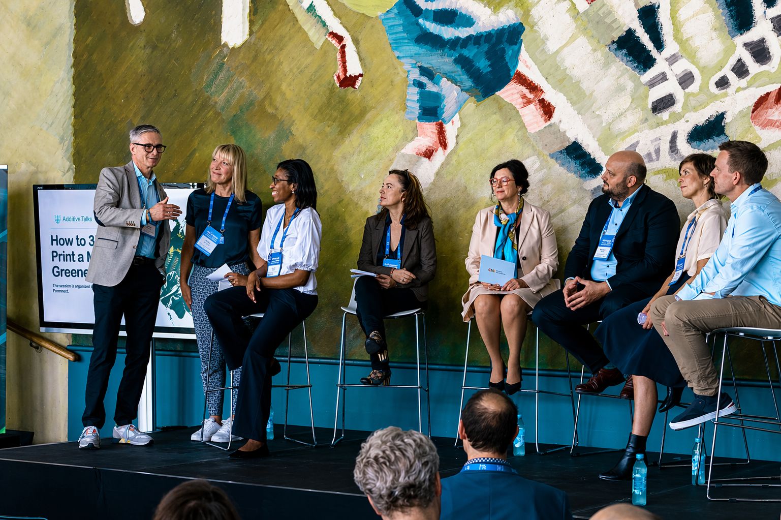 A woman moderating a panel at Danish AM Summit, on sustainability with investors, politicians, and lead AM scientists.